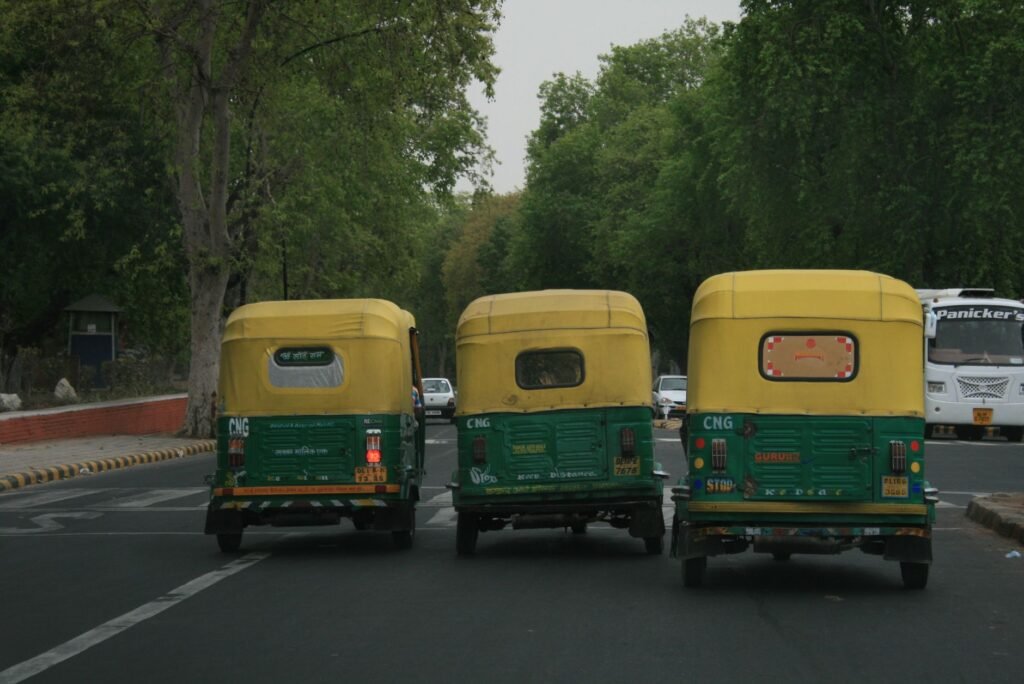Three CNG auto rickshaws on a busy tree-lined street, showcasing urban Indian transportation.