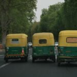 Three CNG auto rickshaws on a busy tree-lined street, showcasing urban Indian transportation.