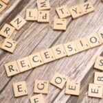 Wooden letter tiles on a wooden surface spell out the word "Recession," symbolizing economic downturn.