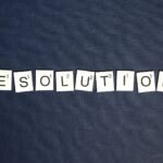 Scrabble tiles spell 'RESOLUTIONS' on a textured dark blue background, capturing a New Year theme.
