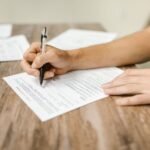 Hand filling out paperwork with a pen, showcasing focus on document completion.