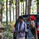 A police officer converses with locals in a lush forest area, standing near a police vehicle.