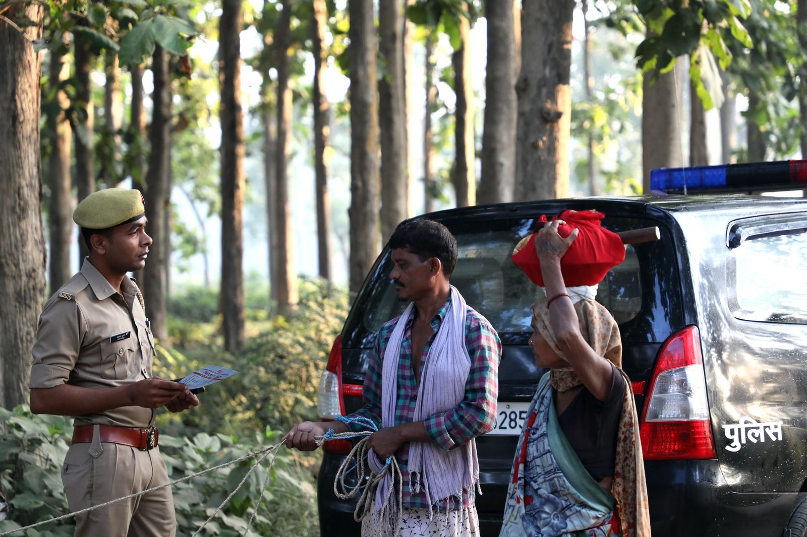 A police officer converses with locals in a lush forest area, standing near a police vehicle.
