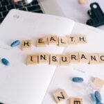 Scrabble tiles spelling 'Health Insurance' on planner with pills and laptop, symbolizing healthcare planning.