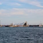 A picturesque view of a bustling maritime center with sailboats and a distinctive architectural landmark.