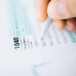 Close-up of a hand using a pen to fill out a tax form 1040, focusing on details.