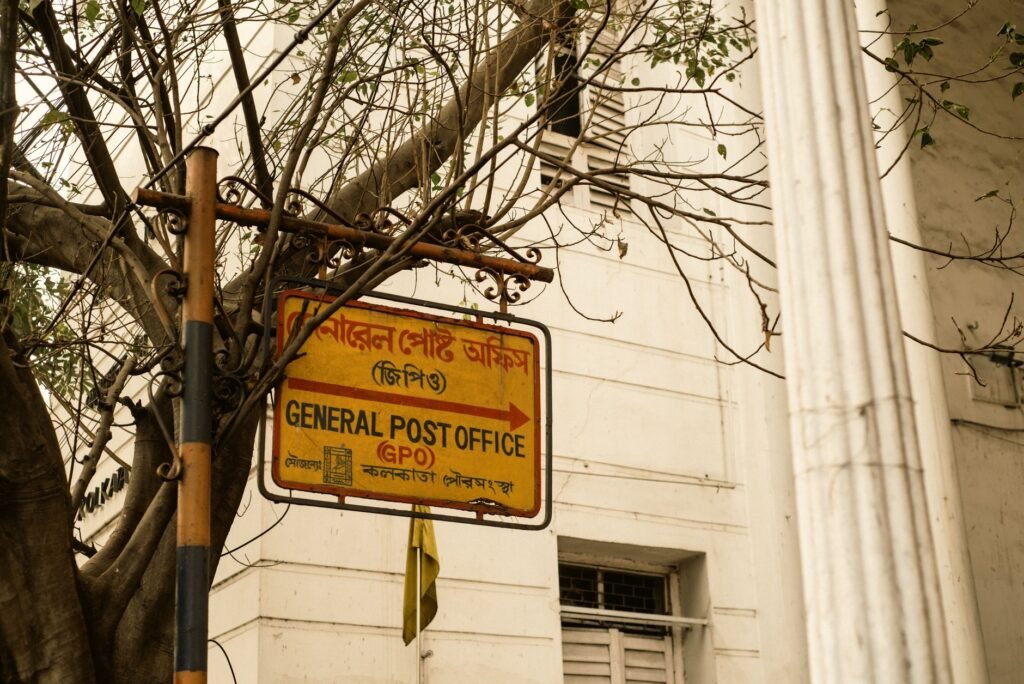 Historic General Post Office sign in Kolkata, India, with tree branches and colonial architecture.