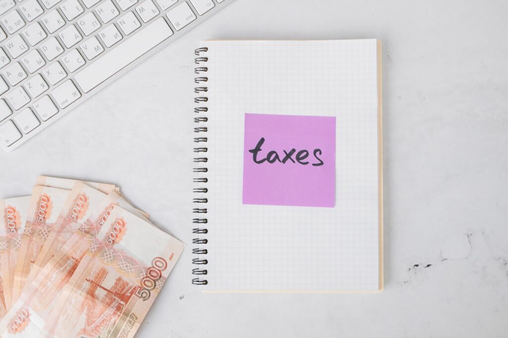 Flat lay image of tax preparation, featuring cash, a notebook, and a computer keyboard on a white surface.
