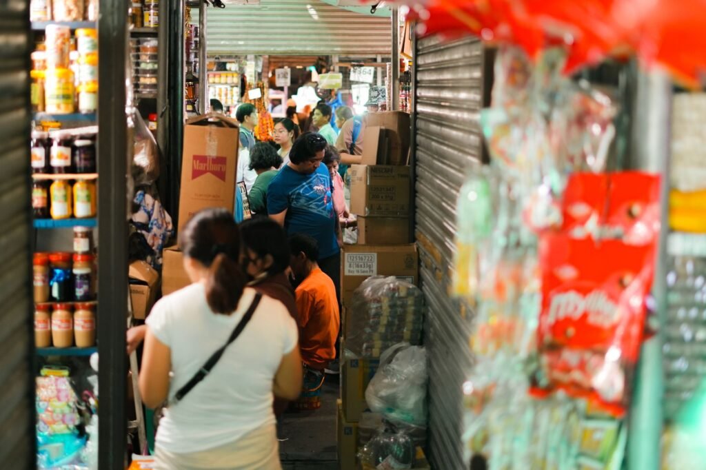 A crowded indoor market with people shopping and stocked shelves.