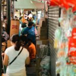 A crowded indoor market with people shopping and stocked shelves.