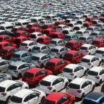 Overhead shot of neatly parked colorful cars in a large outdoor lot under sunlight.