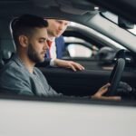 Man examining car interior with salesman at a dealership, highlighting car features.