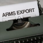 Close-up of a vintage typewriter with the text 'Arms Export' on paper, focusing on journalism and government topics.