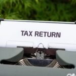 Close-up of a vintage typewriter typing 'Tax Return' on paper outdoors.