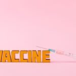 Close-up of a syringe and vaccine vial on a pink backdrop for health concepts.