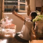Young woman in Lạng Sơn, Việt Nam, enjoys a book amidst flowers in a sunlit room.