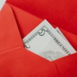 A close-up of a US dollar bill partially visible in a bright red envelope, symbolizing gifting or financial reward.