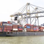 Cargo vessel moored at Kochi, Kerala, India, showcasing global container shipping with cranes in background.