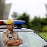 Indian police officer with arms crossed standing by a patrol car outdoors, showcasing authority and law enforcement presence.