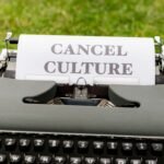 Retro typewriter with 'Cancel Culture' typed paper on grass background outdoors.