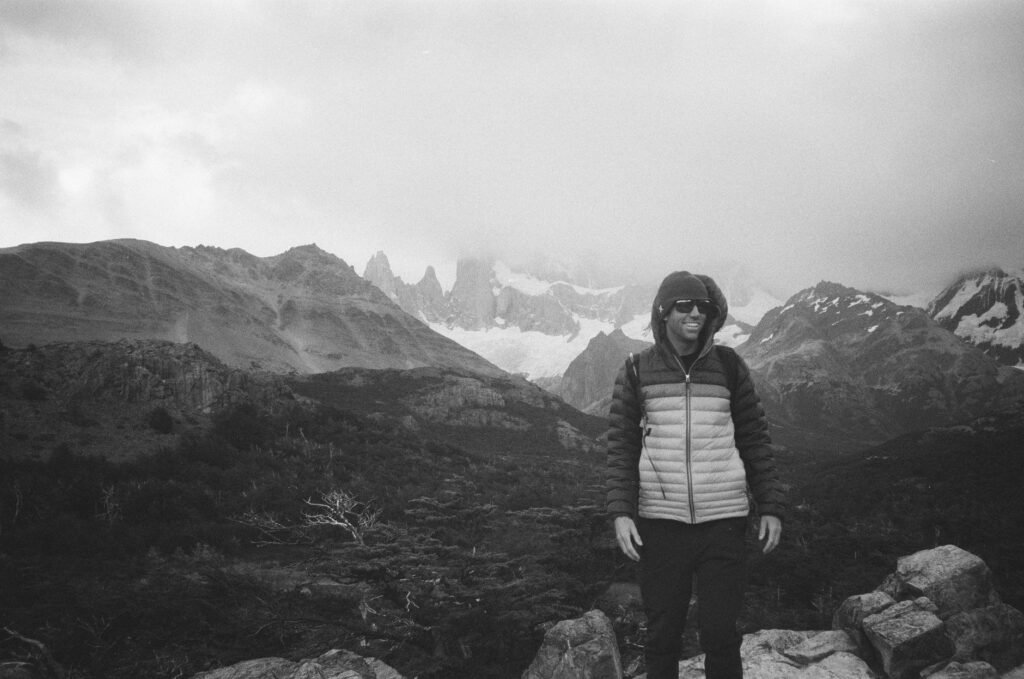 A man smiles while hiking in El Chaltén, Argentina, surrounded by fog and mountains.