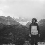 A man smiles while hiking in El Chaltén, Argentina, surrounded by fog and mountains.