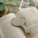 Open book on a green cloth with heart-shaped bookmark and green candle, perfect reading ambiance.