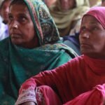 South Asian women in colorful traditional clothing attentively participating in a village meeting.