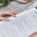 Close-up of hands holding a home insurance document indoors, showing personal details section.