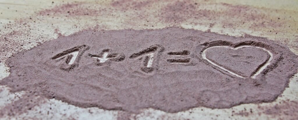 A heart symbol and math equation drawn in sand, symbolizing love.