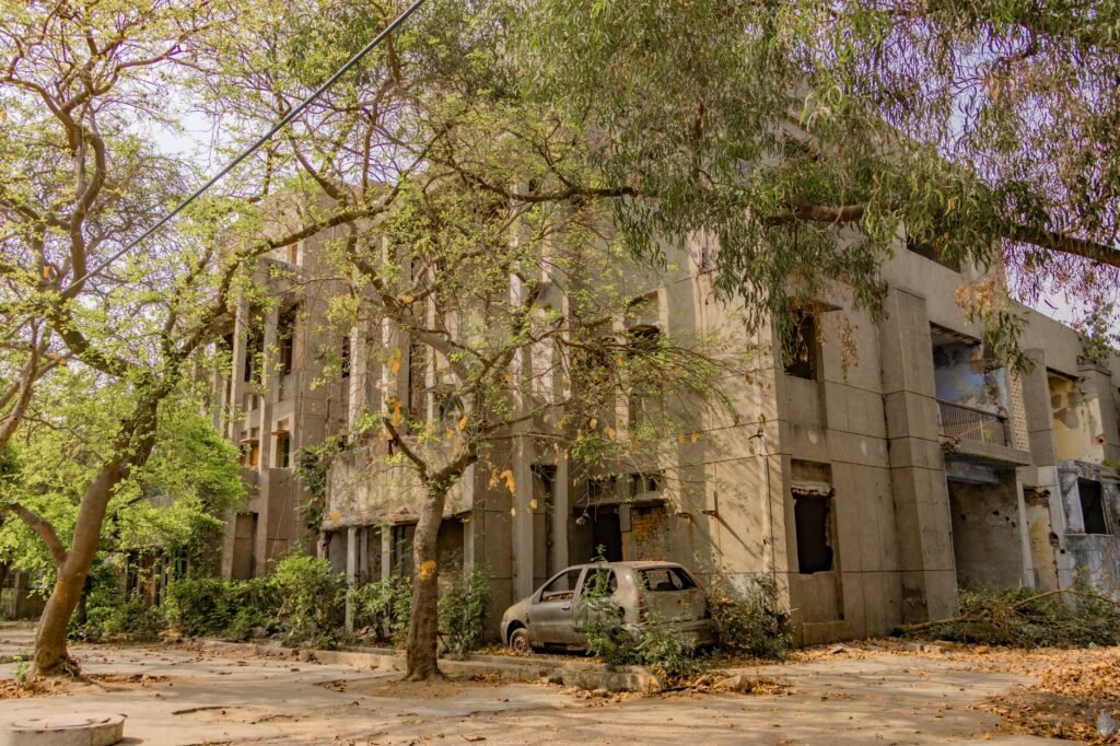 An abandoned building surrounded by lush greenery and an old car, captured in Delhi, India.