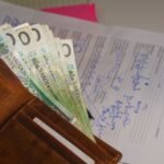 Close-up of a wallet containing Polish Zloty with a signed document in the background, representing financial transactions.