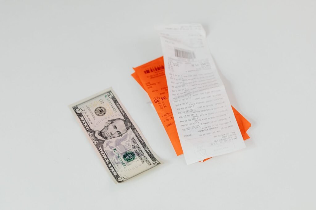 Close-up of a five-dollar bill next to shopping receipts on a white background, ideal for finance and retail themes.