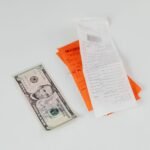 Close-up of a five-dollar bill next to shopping receipts on a white background, ideal for finance and retail themes.