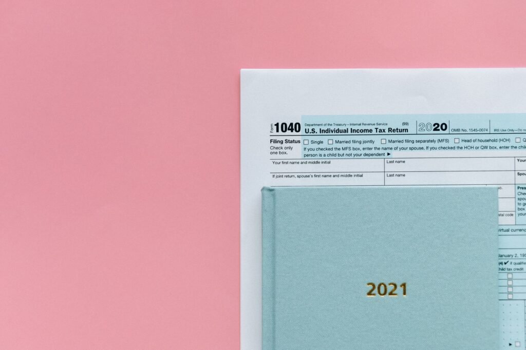 U.S. 1040 tax form with 2021 planner on a pastel pink background, symbolizing tax season.