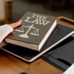 Closeup image of a law book titled 'The Law' on a wooden desk with scales of justice.