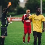 Referee issuing a red card to a soccer player in an outdoor match setting.