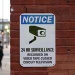 Close-up of a surveillance notice on a brick wall, urban setting.