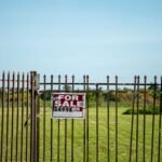 A large plot of land bordered by an iron fence, complete with a 'For Sale' sign in Miami, FL. Ideal for development.