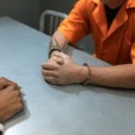 Close-up of prisoner in orange uniform handcuffed during an interrogation.