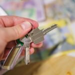 Close-up of keys in hand representing property ownership with blurred financial documents in the background.