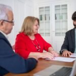 Three business professionals in a meeting, discussing documents and planning strategies indoors.
