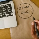 Close-up of hand writing 'Form LLC' on craft paper beside a laptop, indicating business planning.