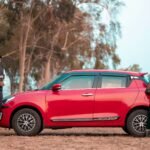 Stylish Indian couple in traditional attire posing by a red car in a rural setting.