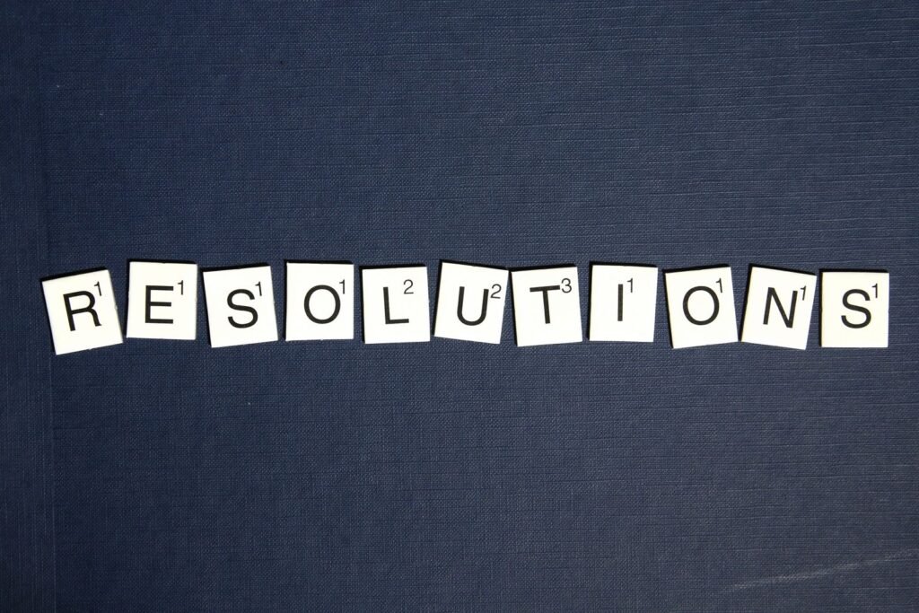 Scrabble tiles spell 'RESOLUTIONS' on a textured dark blue background, capturing a New Year theme.