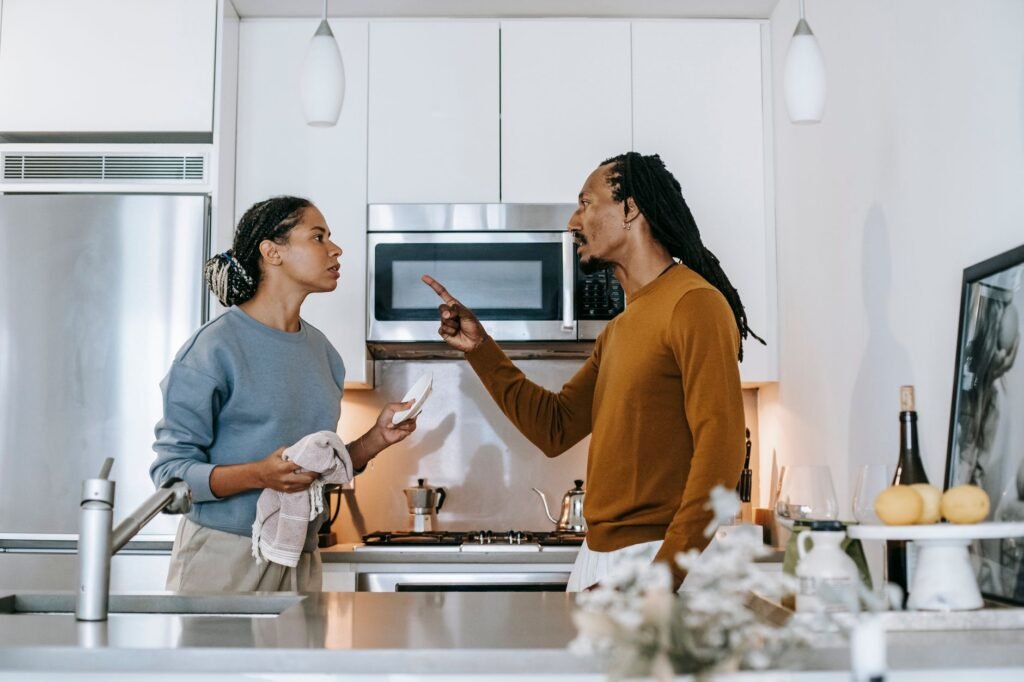Discontented African American male menacing to female partner with finger up while looking at each other during dispute at home