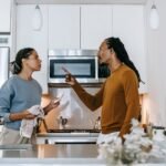 Discontented African American male menacing to female partner with finger up while looking at each other during dispute at home