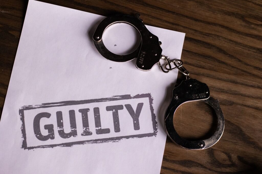 Top view of handcuffs on paper with 'GUILTY' text, symbolizing a verdict or crime.