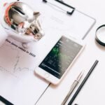 Flat lay of financial tools: chart, smartphone, magnifying glass, and piggy bank.