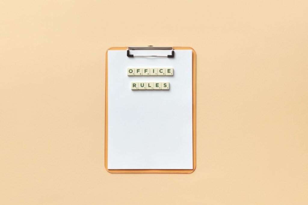 A clipboard with the phrase 'Office Rules' spelled out using Scrabble tiles on a beige background.